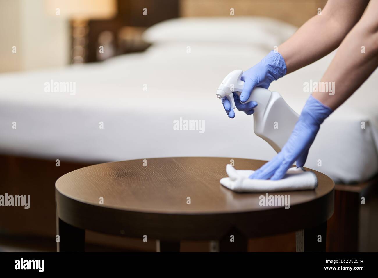 Photo rognée de la femme de ménage pulvérisant le désinfectant sur les meubles pendant le nettoyage de la chambre. Concept de ménage et d'hygiène Banque D'Images