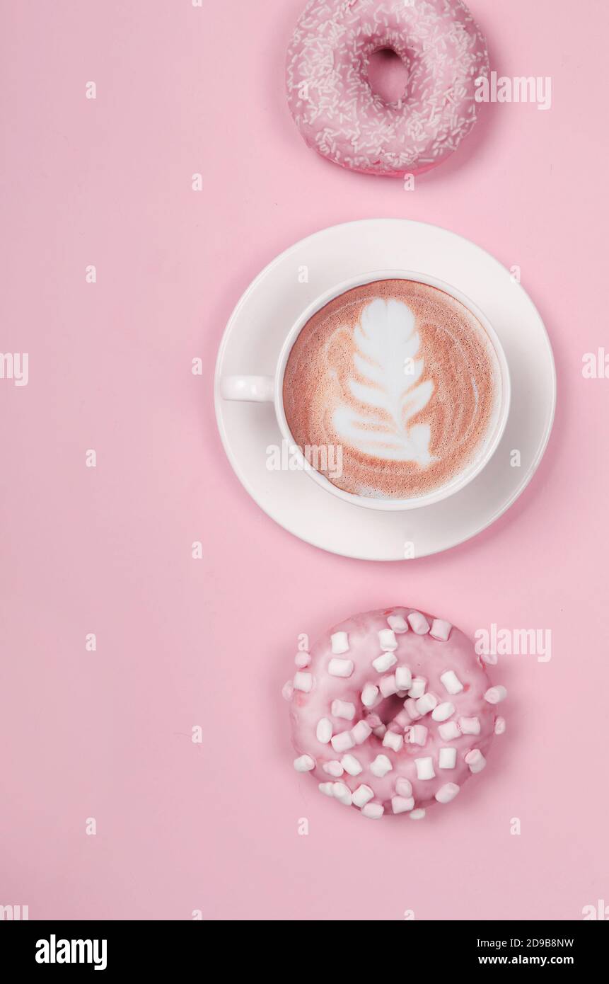 Composition de la couche plate avec deux beignets et une tasse de café sur fond rose Banque D'Images
