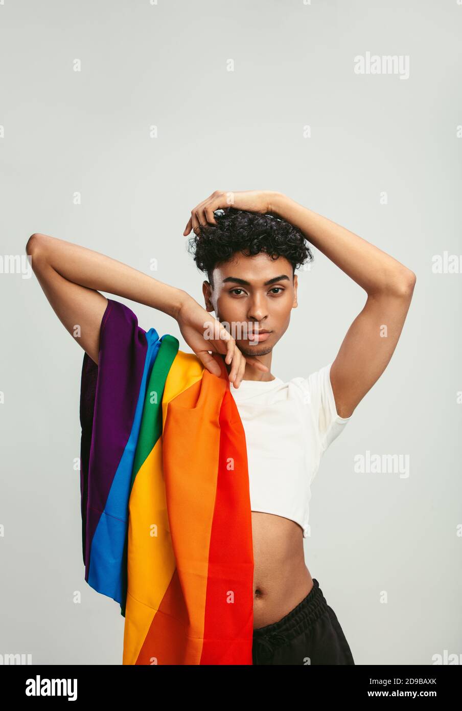 Homme avec un drapeau de fierté posé sur fond blanc. Homme androgyne en crop top posant en studio. Banque D'Images