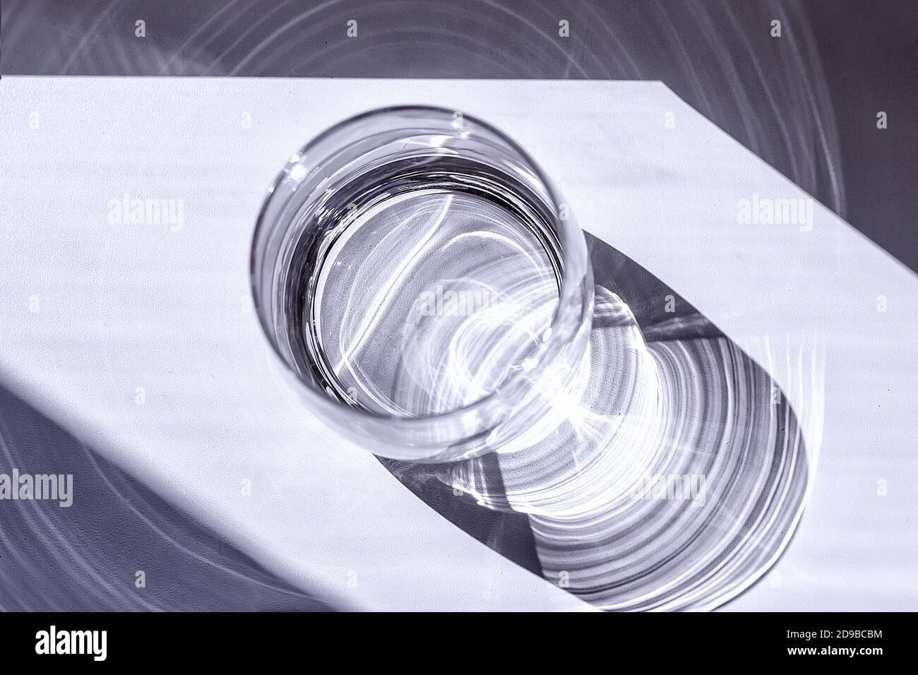 Un verre transparent se tient sur la table dans un rayon de soleil lumineux et crée des ombres intéressantes Banque D'Images