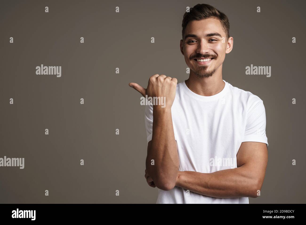 Image d'un gars joyeux et peu rasé souriant et pointant du doigt de côté isolé sur fond gris Banque D'Images