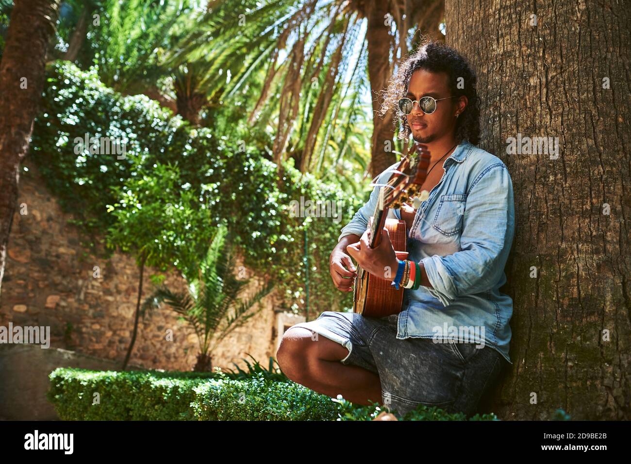 Jeune musicien de guitare classique jouant à l'ombre de quelques arbres dans un parc. Banque D'Images