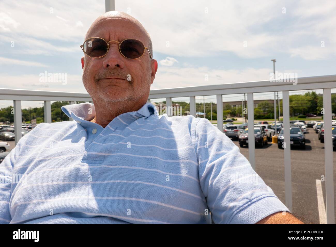 Chauve homme souriant senior citoyen avec chemise à rayures bleues lunettes  de soleil à l'extérieur près d'une clôture blanche Photo Stock - Alamy