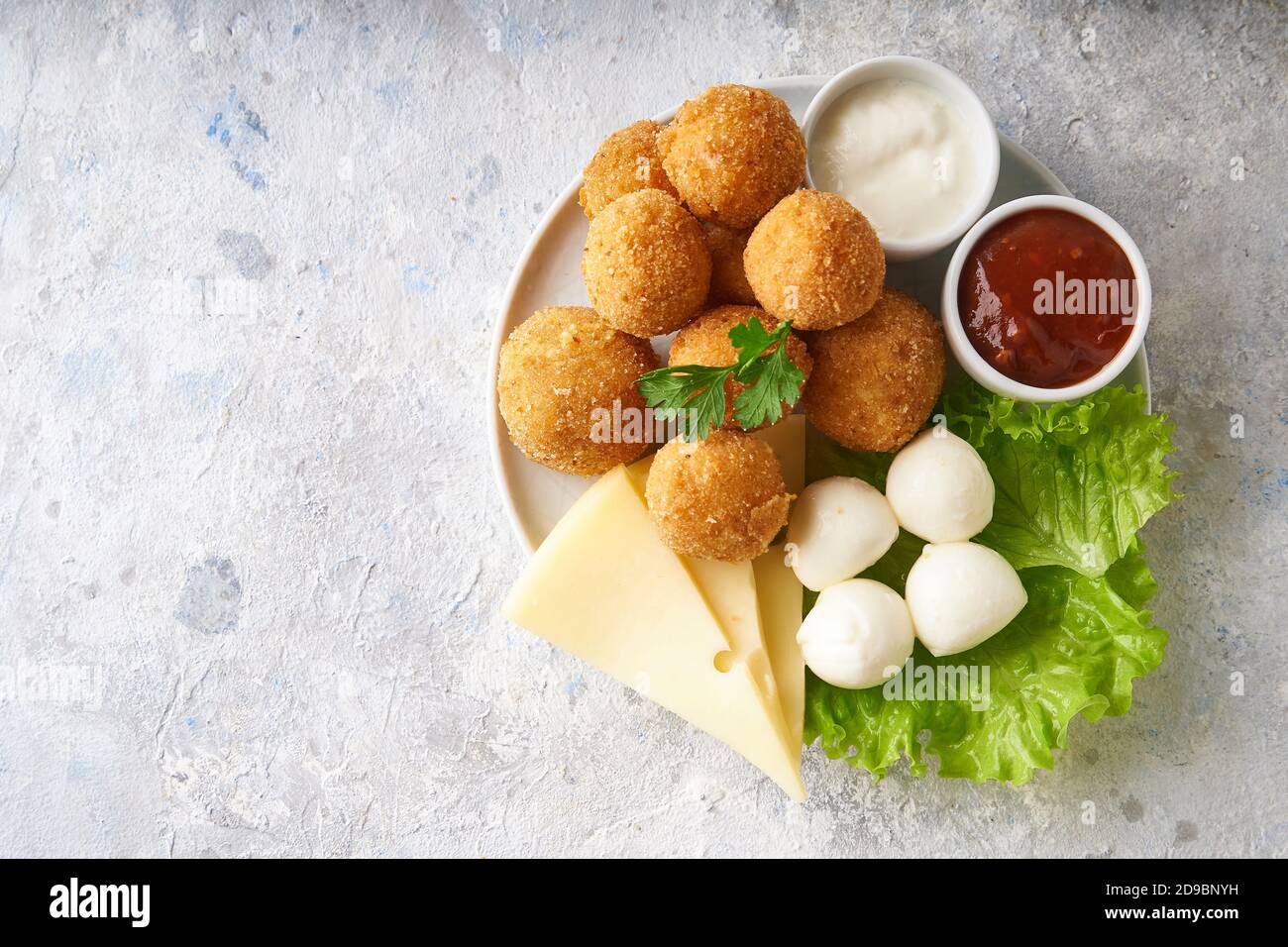 boulettes de fromage, apéritif aux herbes et sauces dans une assiette sur une table grise Banque D'Images