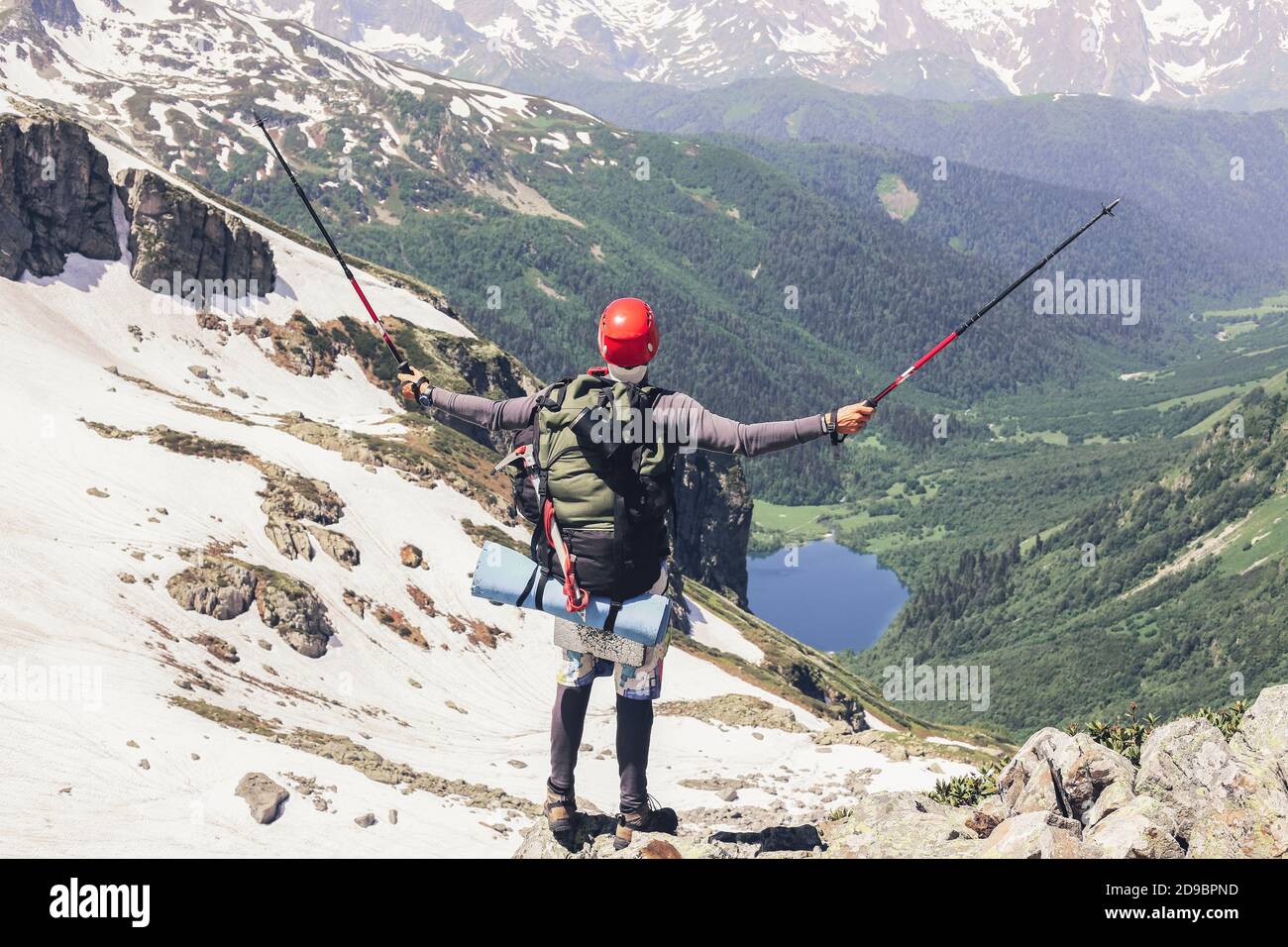Bon touriste avec un grand sac à dos et des bâtons grimpent au sommet de montagne et se réjouit à l'objectif atteint en levant les mains vers le haut par rapport à l'arrière-plan des hautes s. Banque D'Images