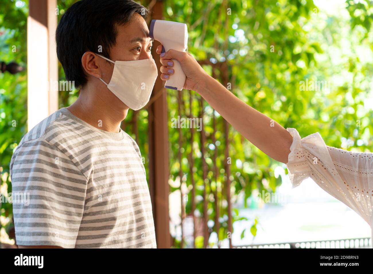 Gros plan à l'aide d'un thermomètre infrarouge numérique médical sur un jeune homme en masque facial pour vérifier et surveiller la température corporelle. Nouvelle vie normale pour dépister les visiteurs afin de prévenir la propagation du coronavirus COVID-19 Banque D'Images