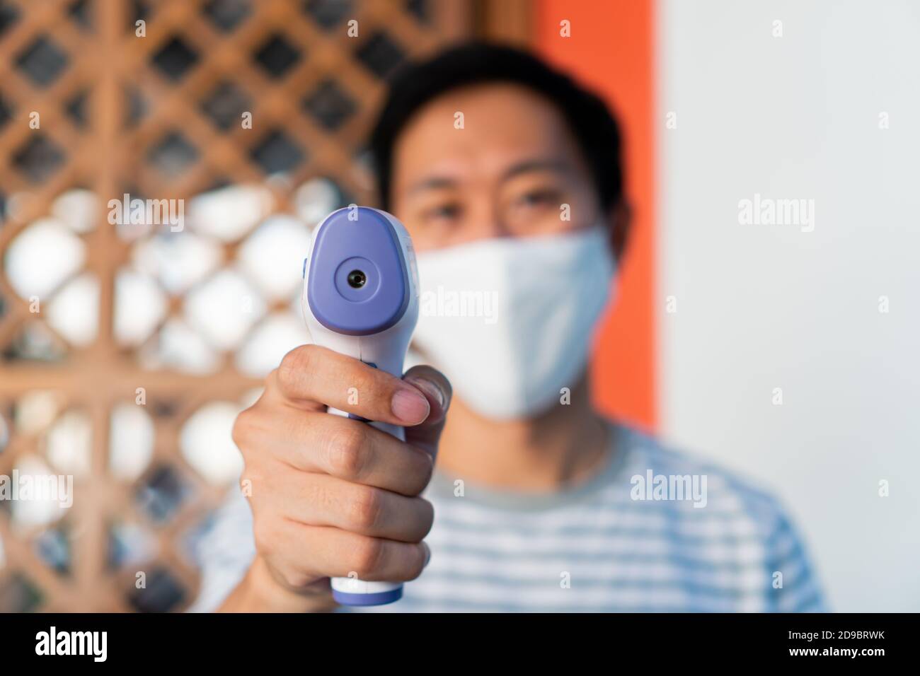 Jeune homme dans un masque facial utilisant un thermomètre numérique infrarouge médical pour vérifier et surveiller la température corporelle. Nouvelle vie normale pour dépister les visiteurs afin de prévenir la propagation du coronavirus COVID-19. Banque D'Images