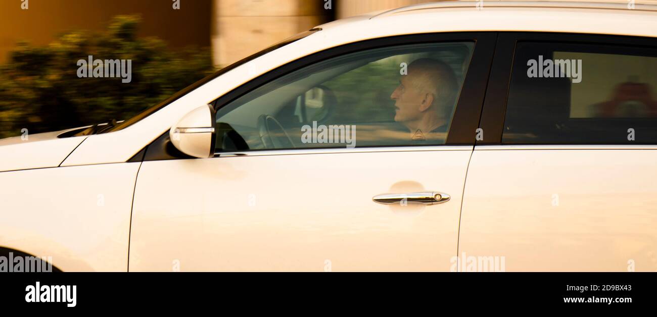 Belgrade, Serbie - 9 octobre 2020 : homme senior, conduisant une voiture blanche dans la rue de la ville, seule, à travers la fenêtre avec des reflets et des flous Banque D'Images