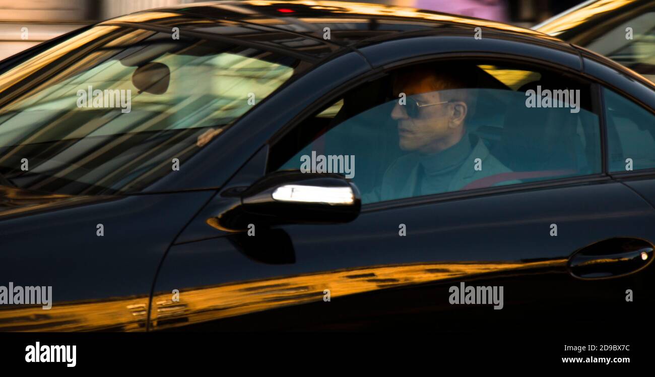 Belgrade, Serbie - 9 octobre 2020 : homme adulte en costume portant des lunettes de soleil conduisant une voiture noire sur la rue de la ville, seule, à travers la fenêtre avec des reflets Banque D'Images
