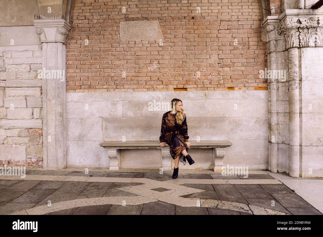 Belle fille avec une robe longue marron et noire, assise sur un banc et regardant sur le côté, à Venise, Italie Banque D'Images