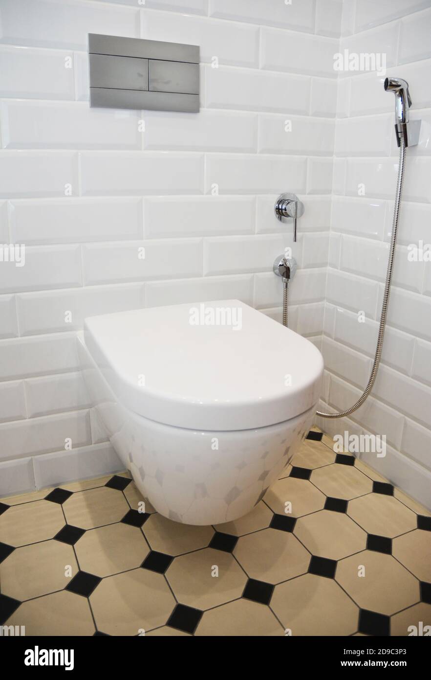 Une salle de toilette rénovée de style rétro avec des murs carrelés de blanc, des carreaux de sol jaune et noir, un bol de toilette en céramique fixé au mur et un bidet à la main Banque D'Images
