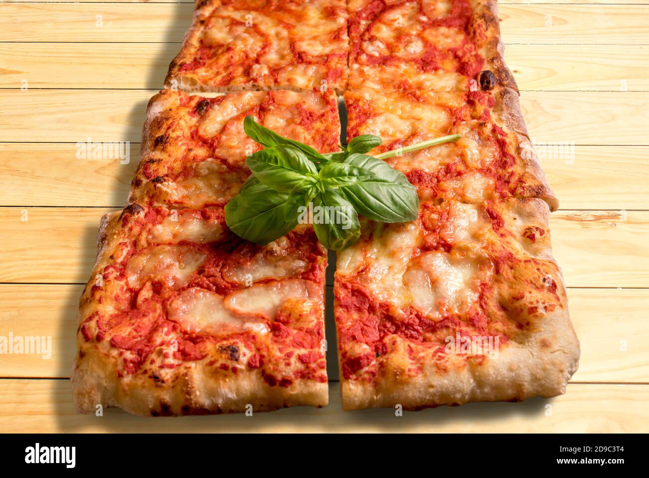 Savoureuse pizza à la coupe carrée avec une belle branche de vert feuilles de basilic sur une surface en bois Banque D'Images