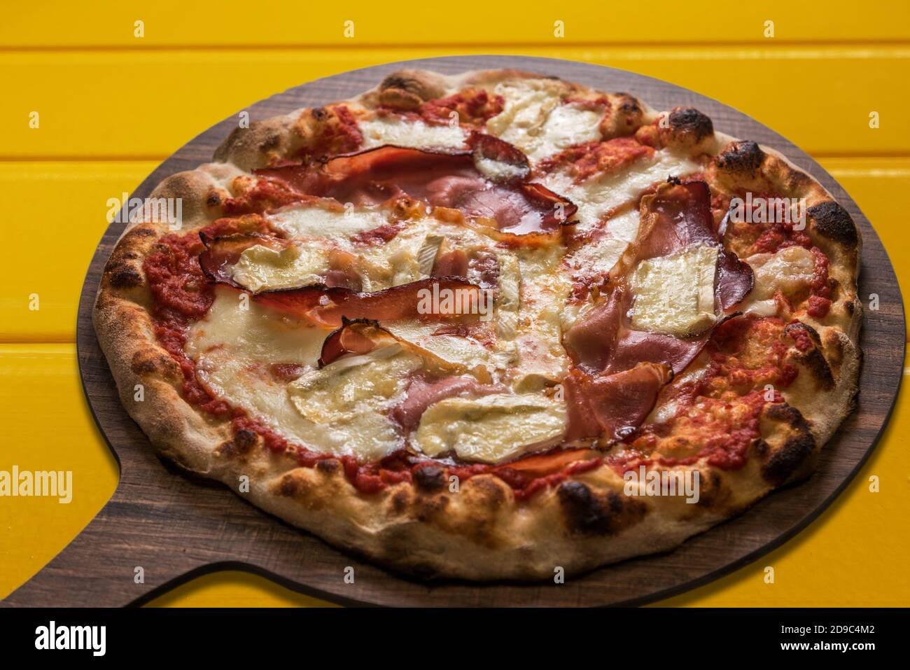 Pizza au bacon ou au fromage blanc et à la brie et à la sauce tomate. Produit italien typique sur une planche à découper en bois sur fond jaune Banque D'Images