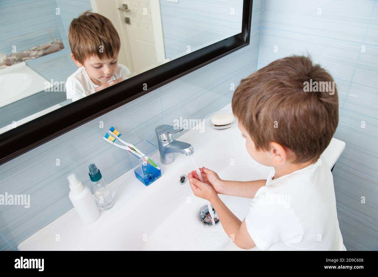 une personne petit caucasien santé mignon enfant en chemise blanche se laver les mains sous l'eau douce dans un lavabo bleu salle de bains à la maison Banque D'Images