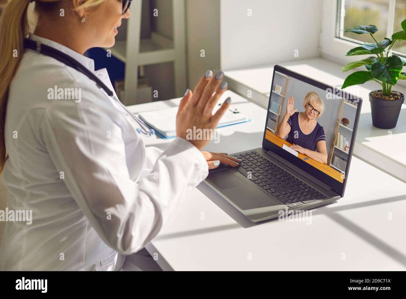 Le médecin agite la main sur l'écran d'un ordinateur portable pour dire bonjour à l'aîné femme lors de la consultation en ligne Banque D'Images