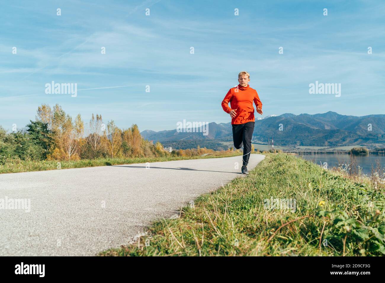 Homme vêtu d'une chemise à manches longues rouge qui court sur la route asphaltée avec fond de montagne. Activités sportives et un concept de style de vie sain im Banque D'Images