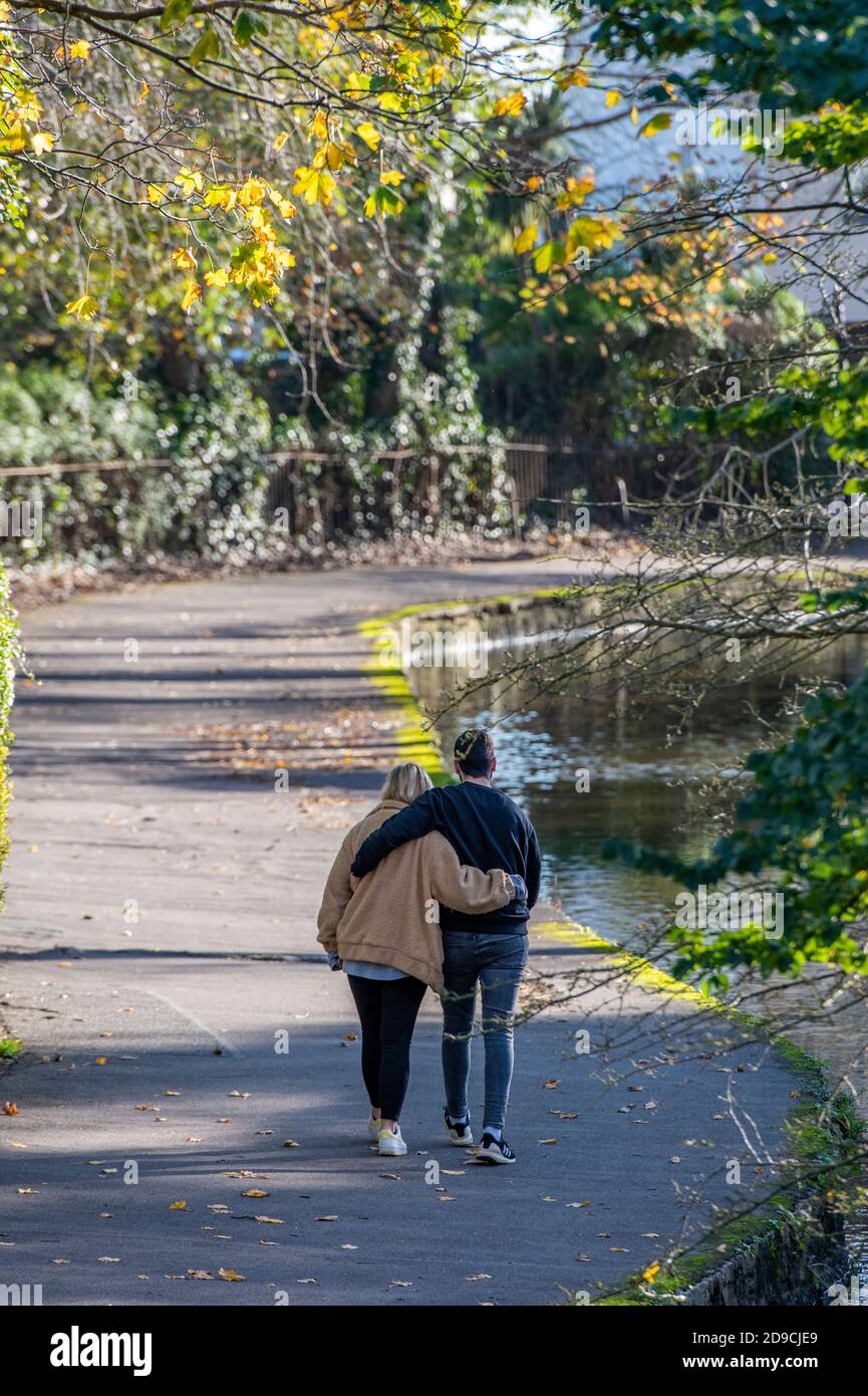 Un jeune couple bras dans le bras marchant le long d'une rivière sous les arbres d'automne lors d'une journée ensoleillée à Christchurch dans dorset. Banque D'Images