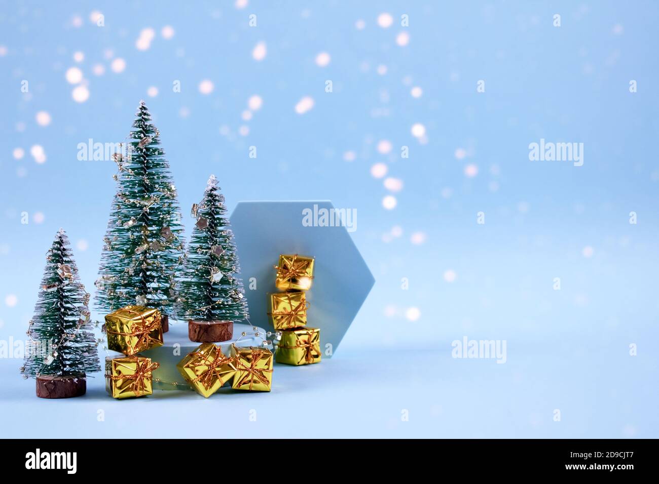 Composition de Noël et du nouvel an avec arbre du nouvel an, boîtes de cadeaux dorées, décorations et lumières de bokeh sur fond bleu pastel avec espace publicitaire Banque D'Images