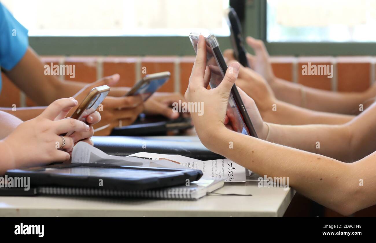 Une table d'élèves du secondaire qui tiennent tous plusieurs appareils numériques tels que des téléphones et des tablettes pendant une leçon de classe. Éducation contemporaine et conn Banque D'Images