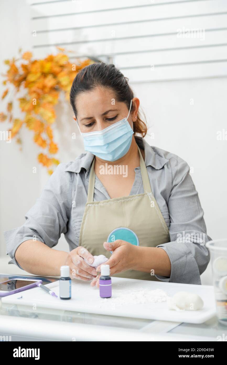 Chef pâtissier travaillant avec fondant pour décorer un gâteau - Femme cuisinant avec masque - femme peignant de l'argile avec des teintures Banque D'Images