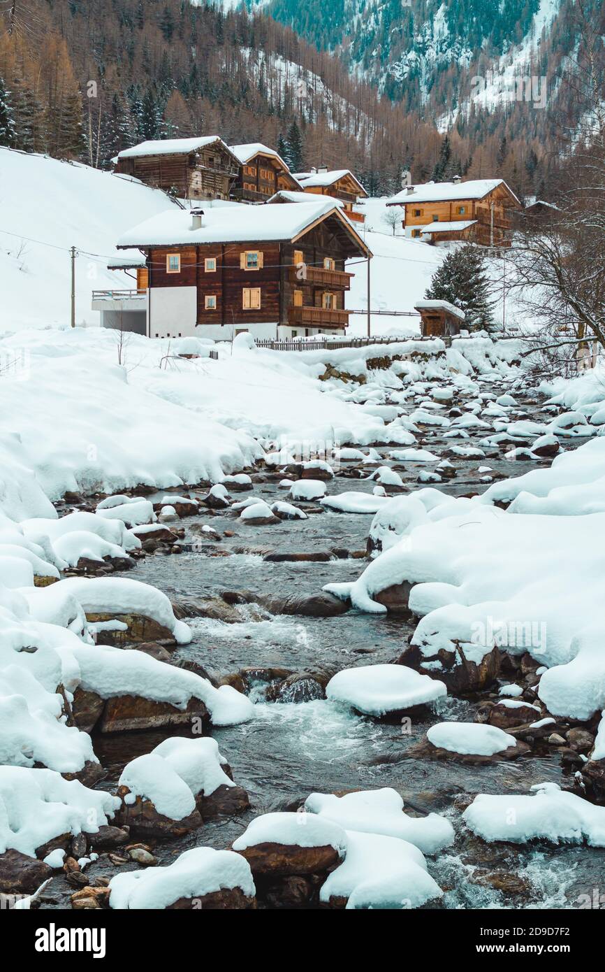 Ruisseau recouvert de glace et de neige par une froide journée d'hiver en face des cabines traditionnelles en bois du petit village de montagne St. Gertraud à Ultental, Tyrol du Sud/ Banque D'Images