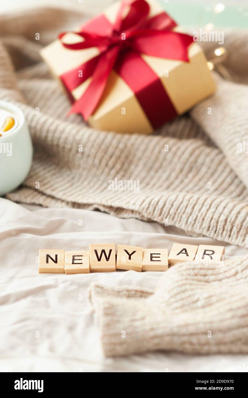 inscription nouvel an sur tissu beige froissé, boîte cadeau avec ruban rouge, guirlande sur pull beige sur fond. carte du nouvel an festive et confortable, Banque D'Images