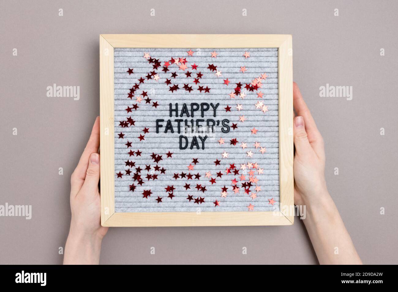 Les mains tiennent le lettrage avec citation heureux fête des pères sur fond gris. Concept de vacances avec étoiles rouges confetti. Banque D'Images