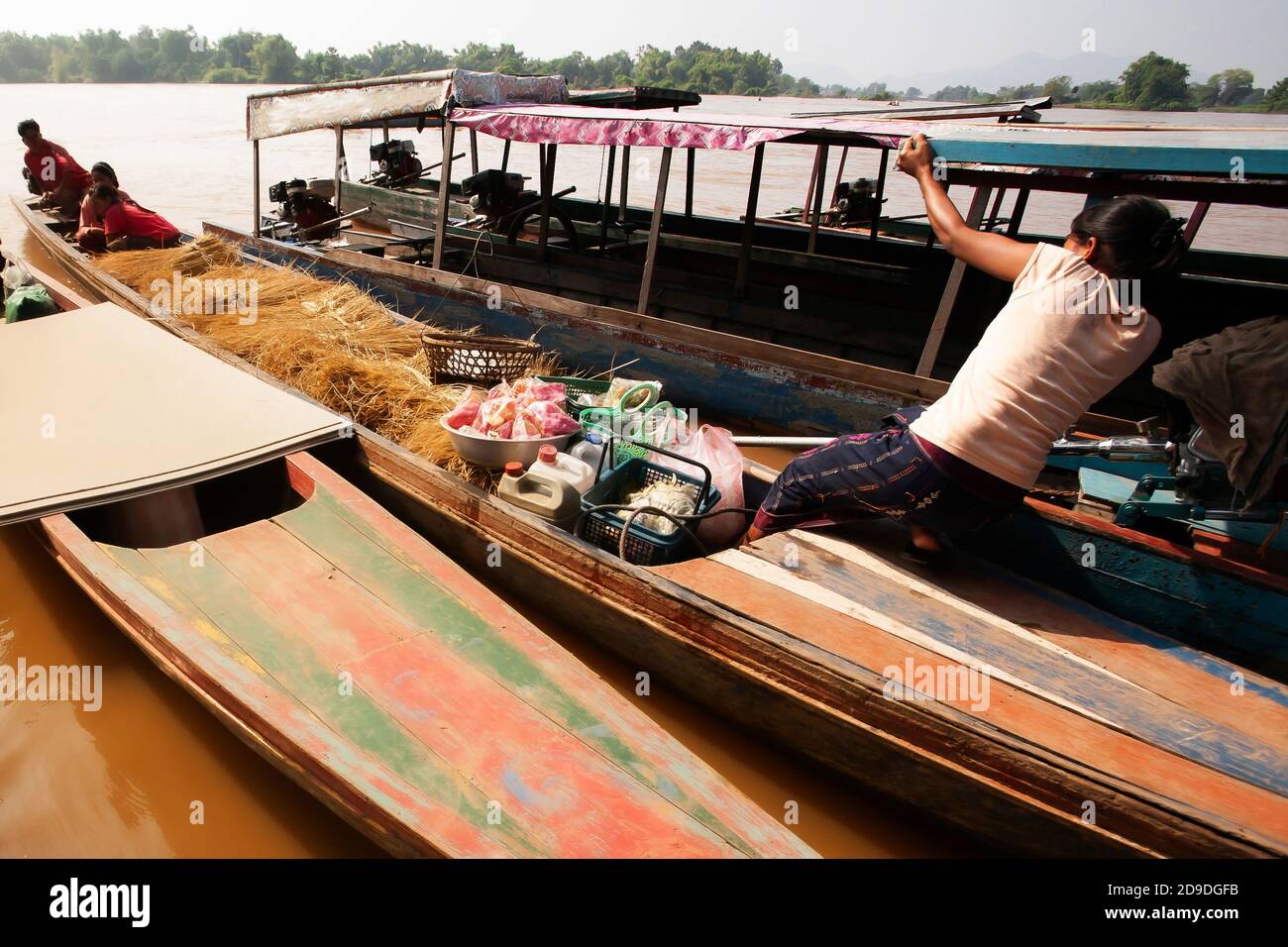 Femme laotienne tenant le toit du bateau tout en prenant un ferry traditionnel en bois à un quai près de si Phan Don ou quatre mille îles, Mékong, Laos. Banque D'Images
