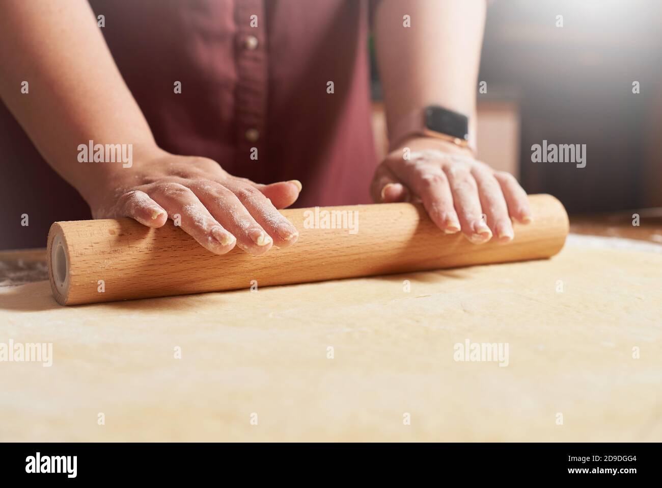 Les mains des femmes roulent la pâte crue avec un rouleau broche Banque D'Images