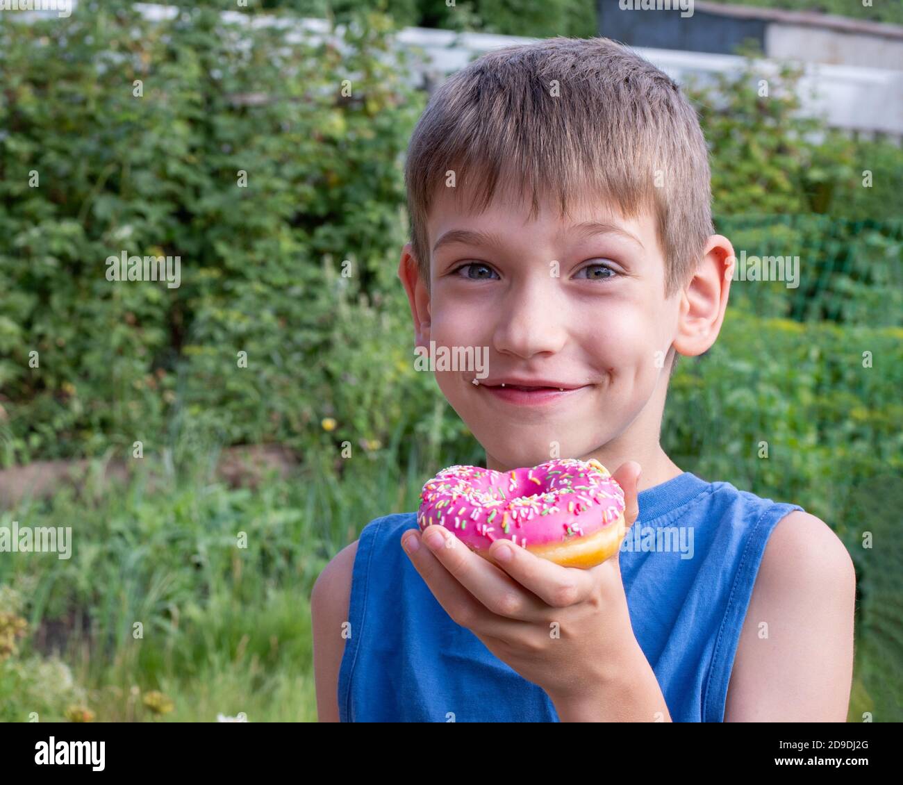 Un enfant heureux mange un beignet rose dans le parc. Concept alimentaire malsain, grignotage de nourriture douce. Les enfants adorent les aliments sucrés Banque D'Images