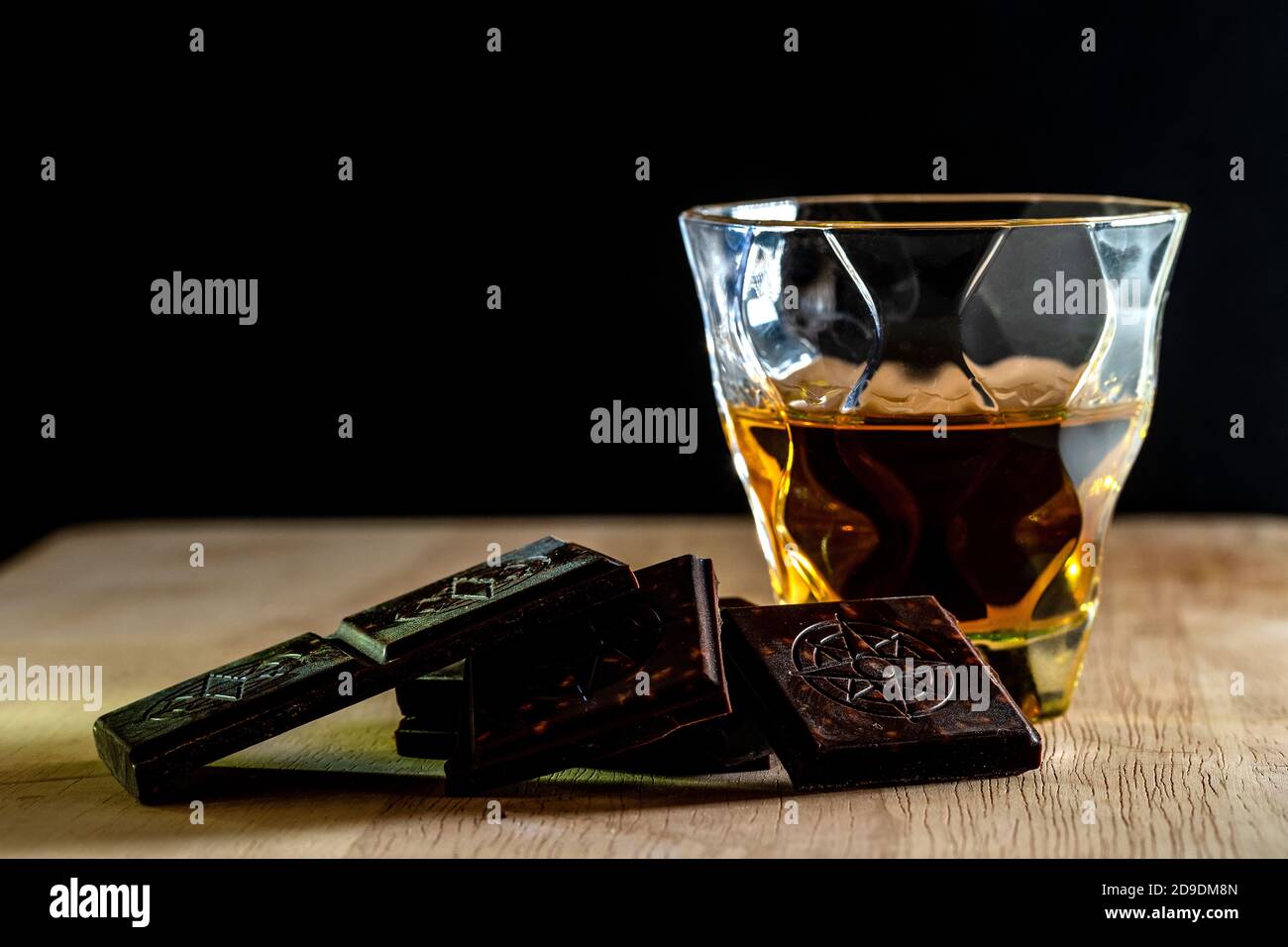 Un verre de brandy. Whisky. Cognac avec morceaux de chocolat noir sur table en bois et fond noir. Banque D'Images