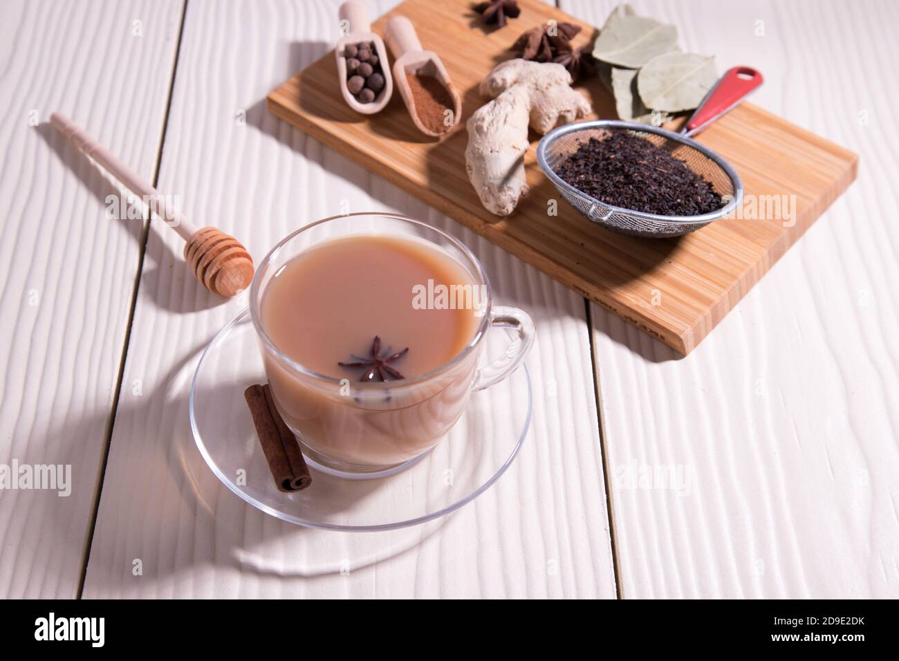 Une tasse de thé indien chaud masala, cuillères aux épices, gingembre, anis sur une planche à découper, sur fond blanc. Orientation horizontale. Banque D'Images