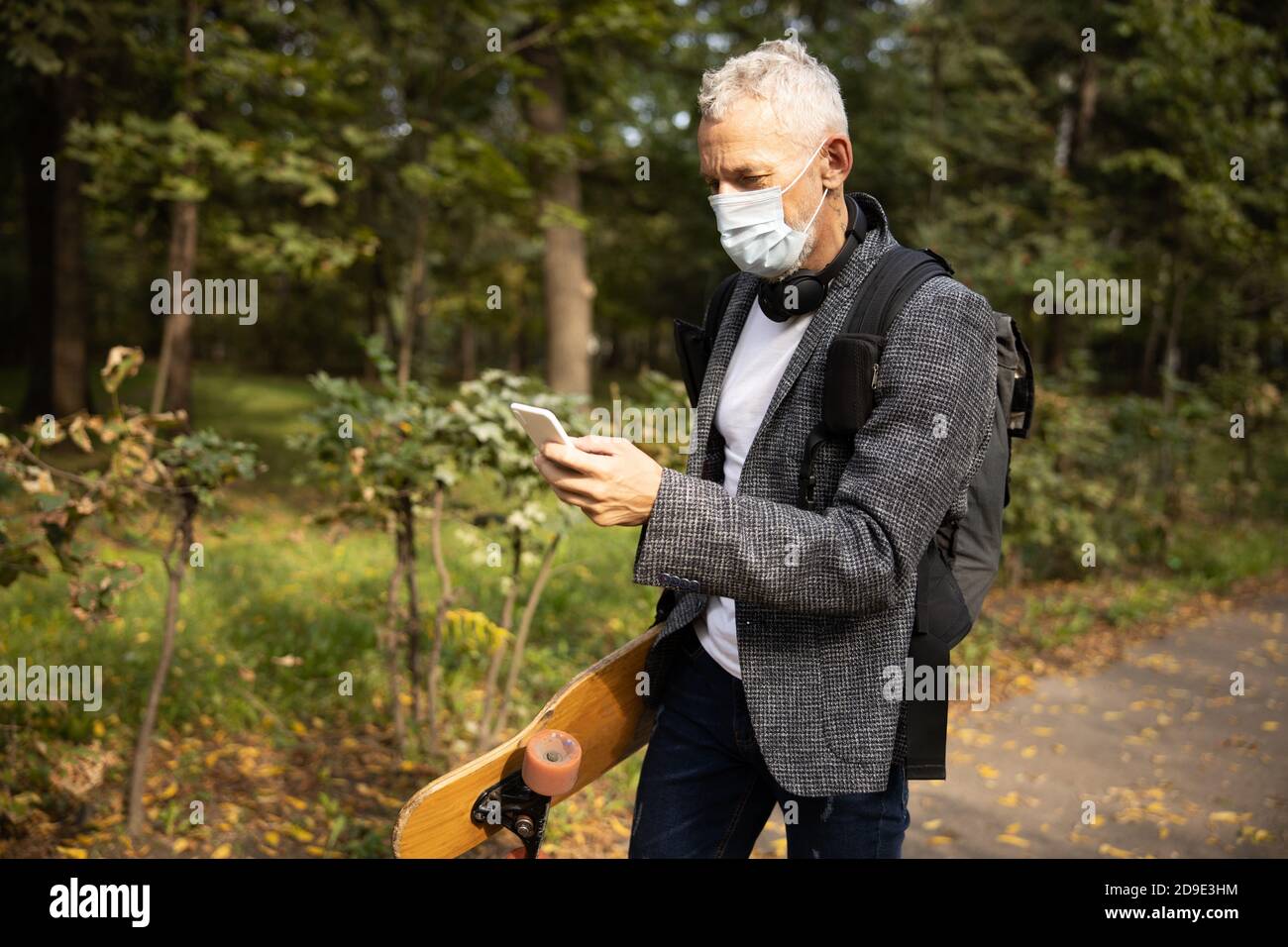 Homme dans le masque en utilisant le smartphone à pied Banque D'Images
