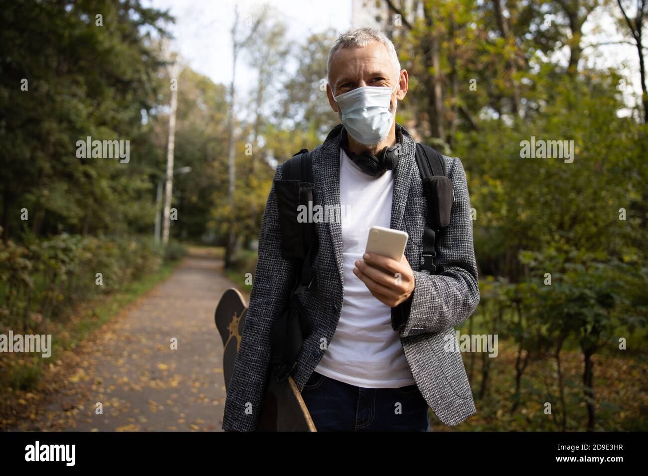 Joyeux homme mature en masque marchant avec smartphone en bois Banque D'Images