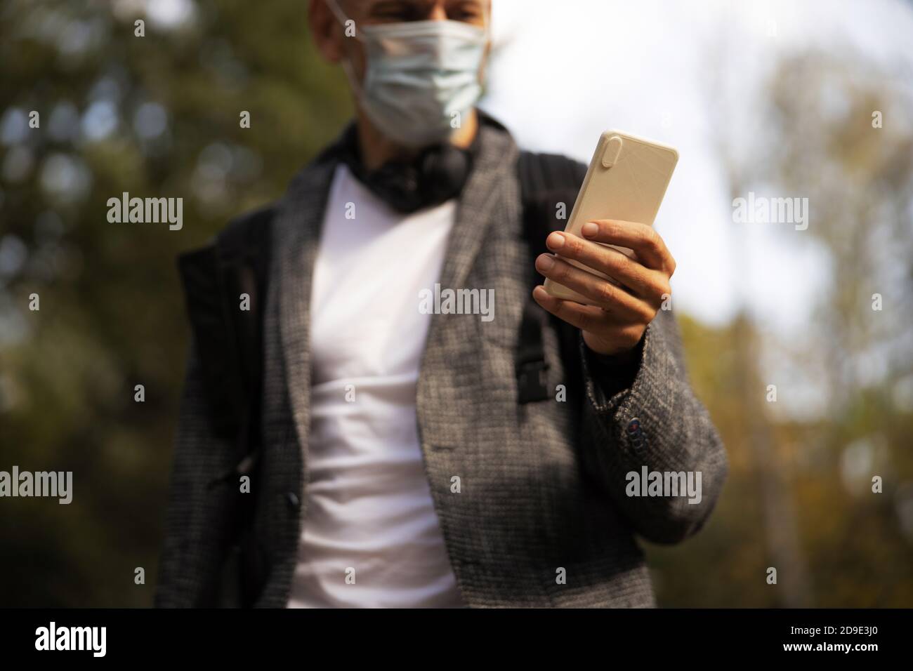 Homme dans un masque stérile utilisant un smartphone à l'extérieur Banque D'Images