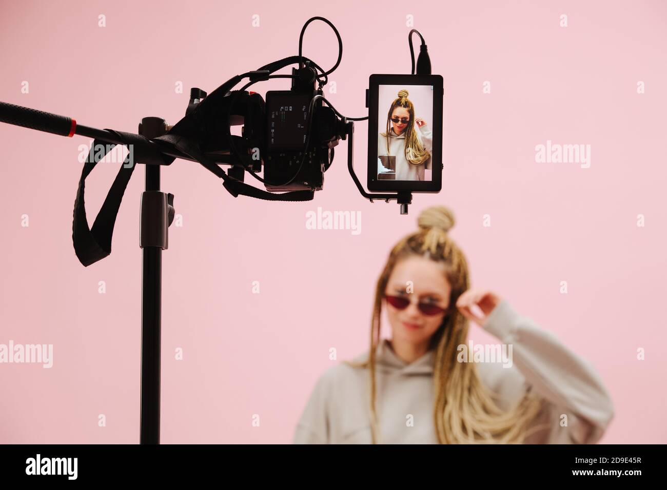 Caméra avec moniteur de terrain filmant femme élégante avec blonde afro tresses sur rose Banque D'Images