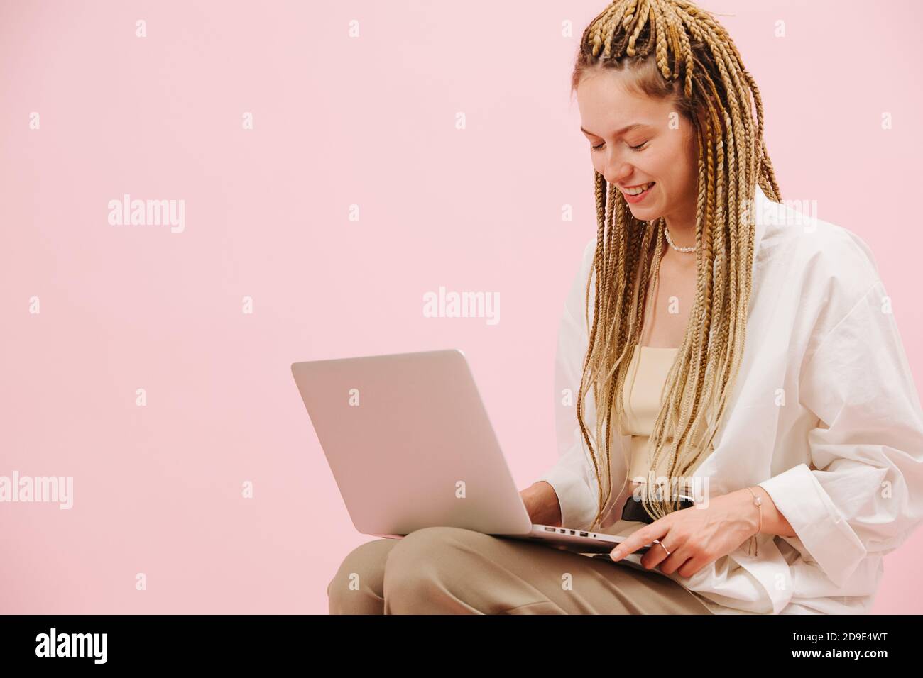 Bonne jeune femme avec des tresses blondes afro élégantes un ordinateur portable plus rose Banque D'Images