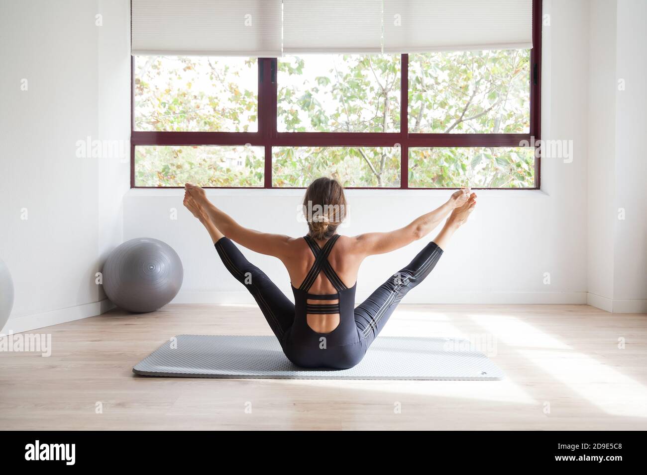 Femme sportive pratiquant le yoga en tenant ses pieds dans un brillant loft studio Banque D'Images