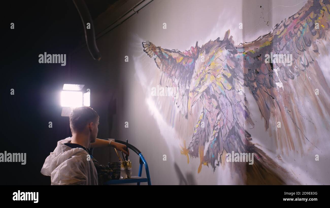 Concepteur de l'artiste dessine un aigle sur le mur. Décorateur artisan photo peintures à l'acrylique couleur d'huile. Peintre peintre vêtu de couche de peinture. À l'intérieur. Banque D'Images