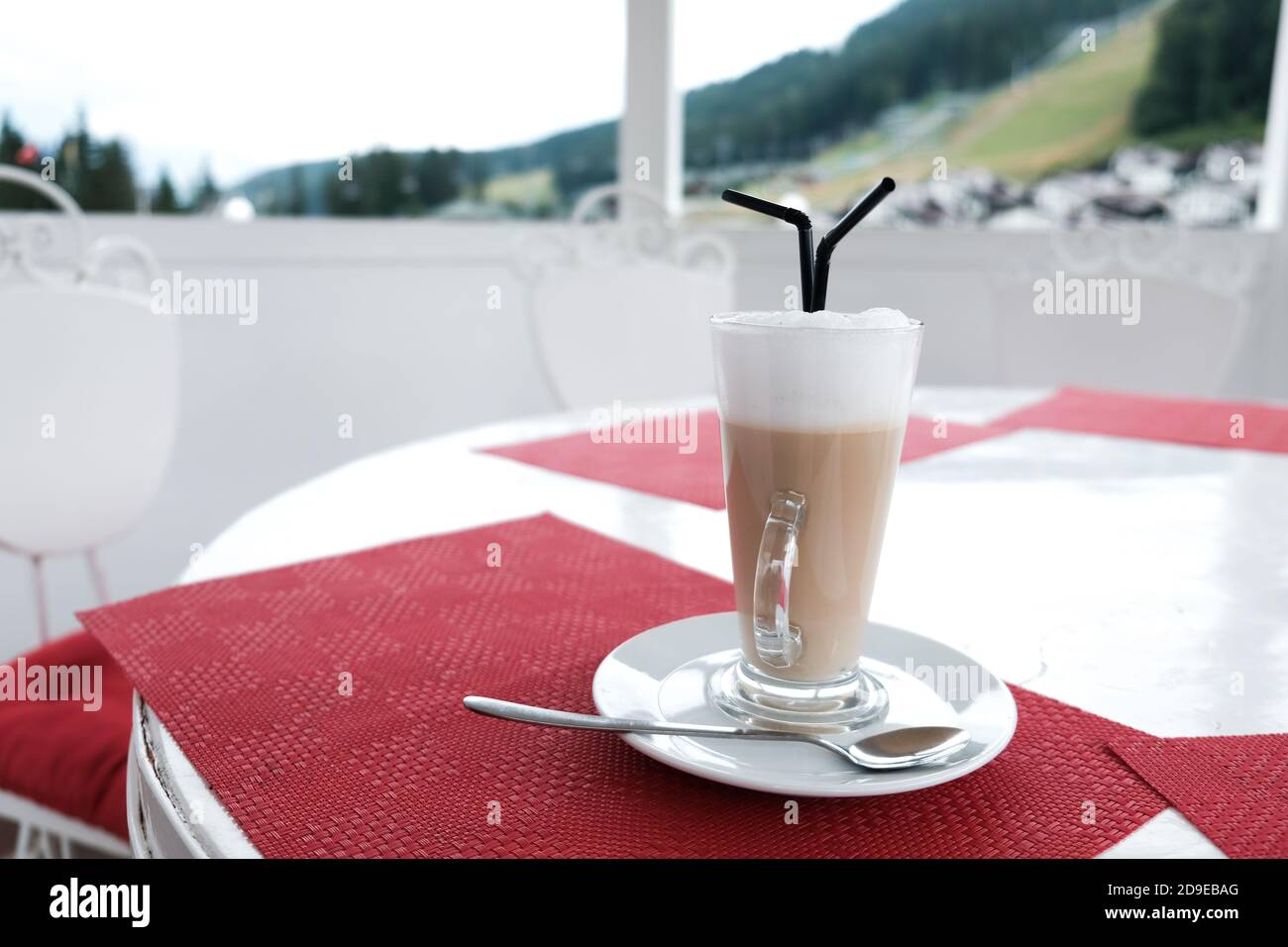 Une tasse de café latte en verre avec deux pailles en plastique sur une table à l'extérieur. Il sert des boissons caféinées dans une cafétéria. Service de restauration magnifique. Banque D'Images