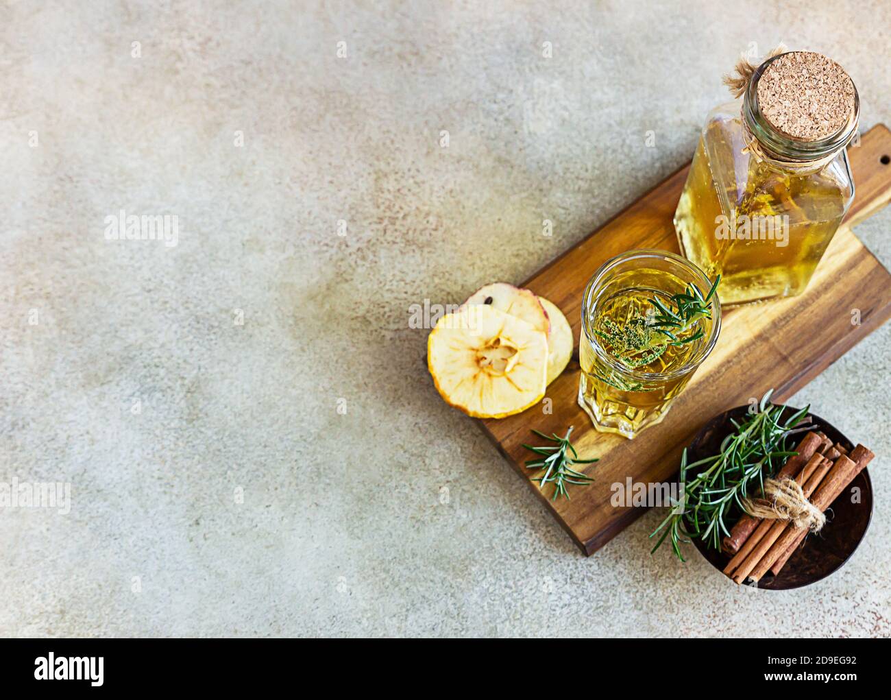 Cidre de pomme ou de poire en grand verre et bouteille de romarin, cannelle et chips de fruits secs, fond en béton léger. Vue de dessus. Banque D'Images