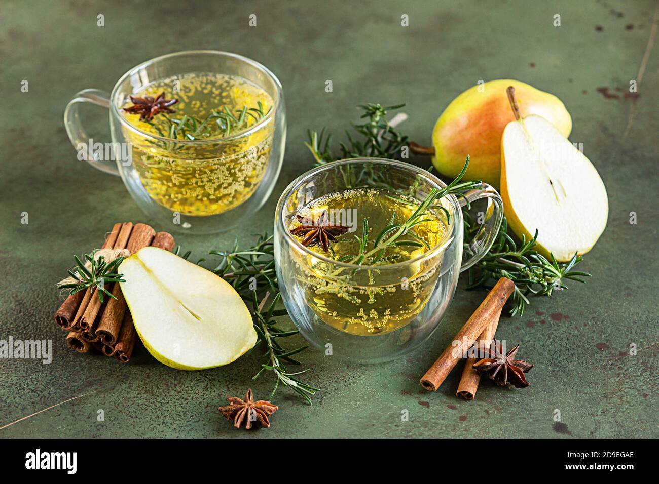 Poire chaude épicée ou cidre de pomme avec cannelle, anis et romarin. Boissons traditionnelles d'automne ou d'hiver. Fond en béton vert. Banque D'Images