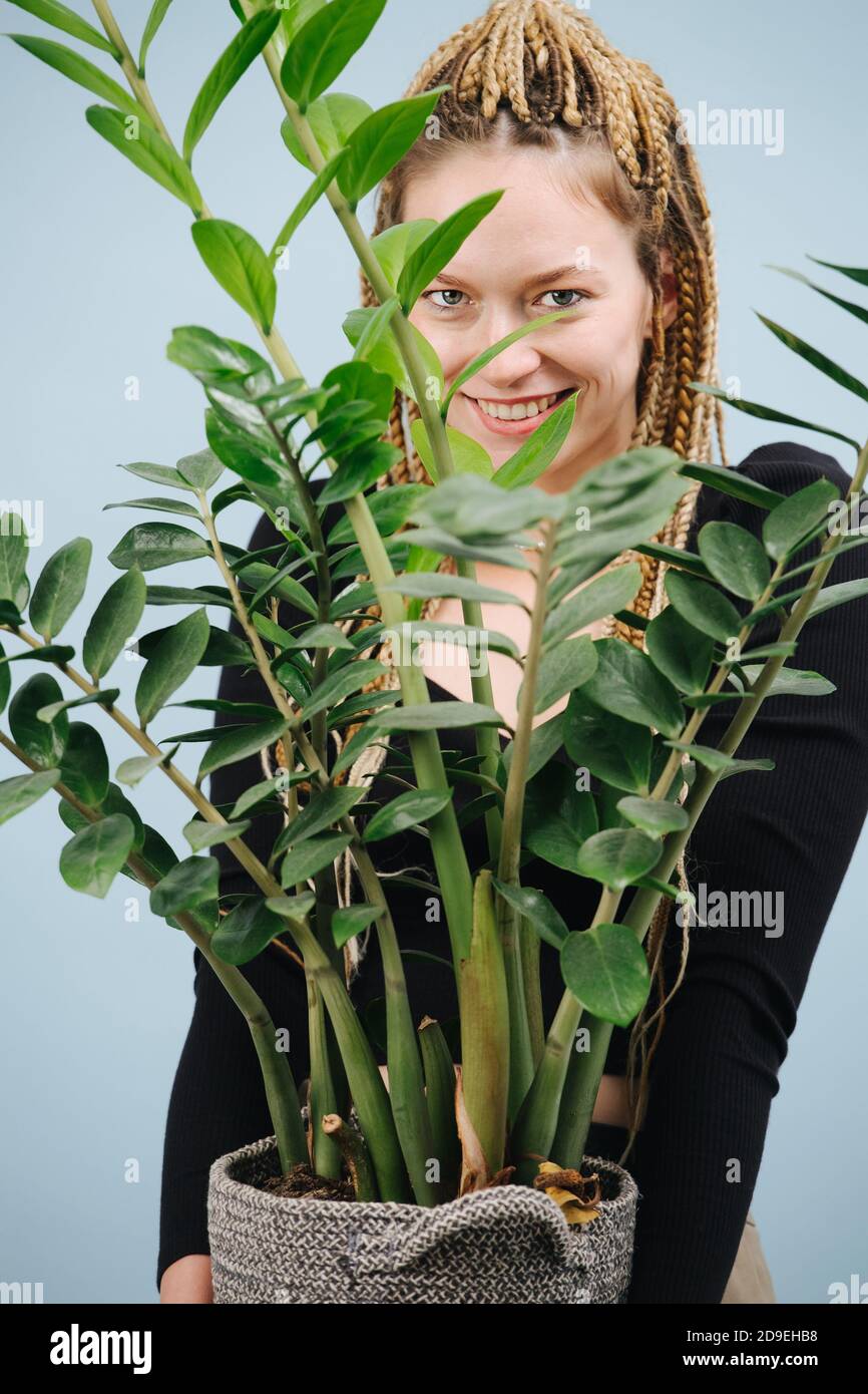 Femme flirty avec les tresses afro blondes élégantes debout avec pot plante entre les mains Banque D'Images