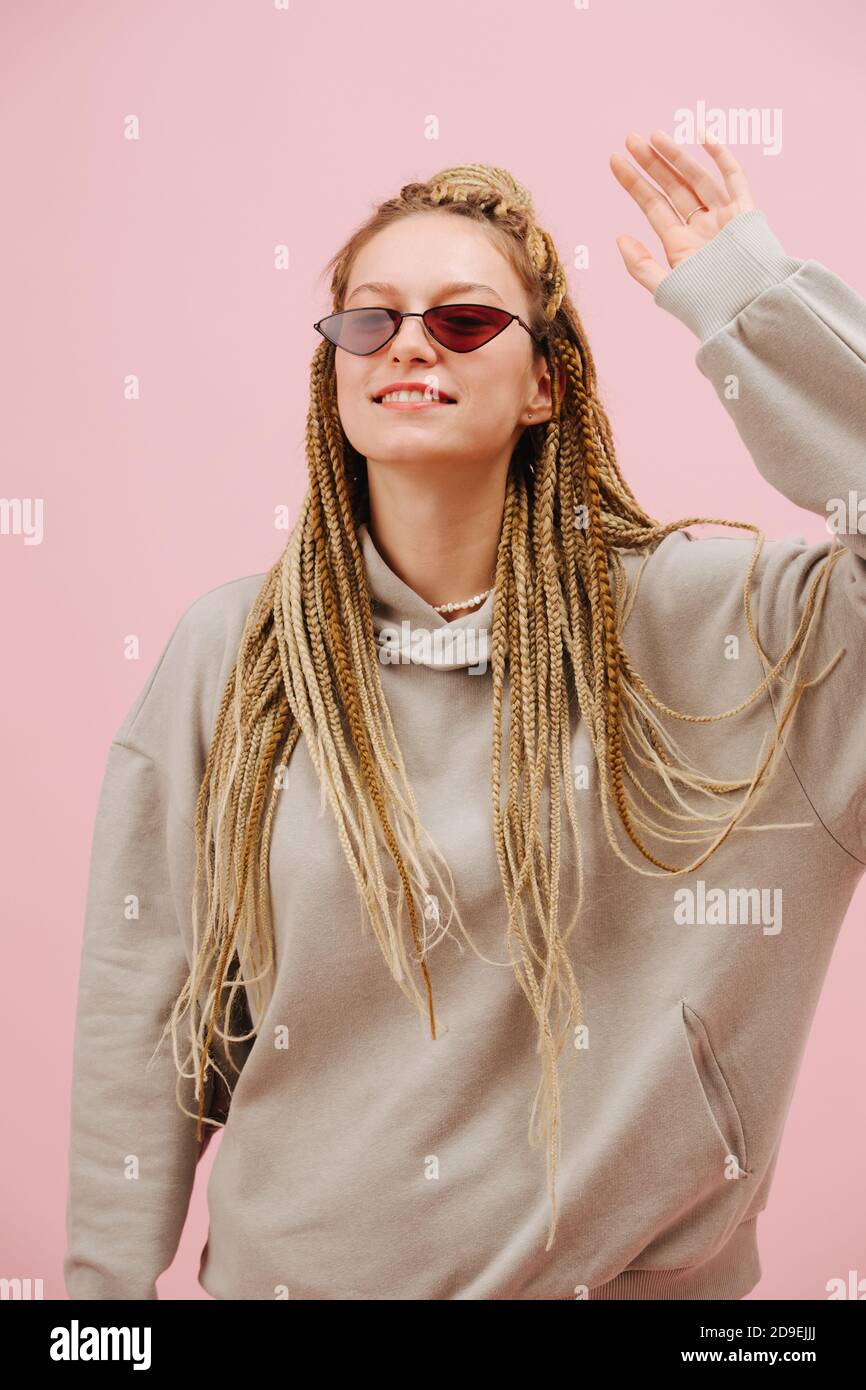 Femme sympathique dans des lunettes de soleil avec blonde élégant braids afro plus fond rose Banque D'Images