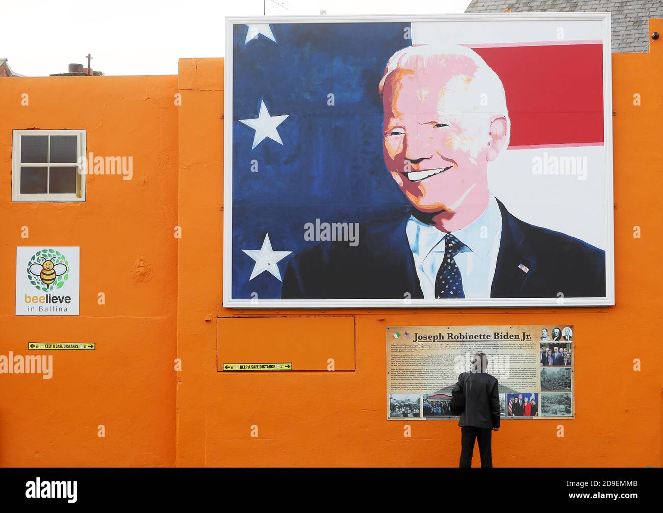 Un homme s'arrête pour lire une plaque sous une fresque du candidat à la présidence des États-Unis Joe Biden dans sa maison ancestrale de Ballina, Co. Mayo, Irlande, où il s'est rendu en juin 2016 en tant que vice-président. Banque D'Images