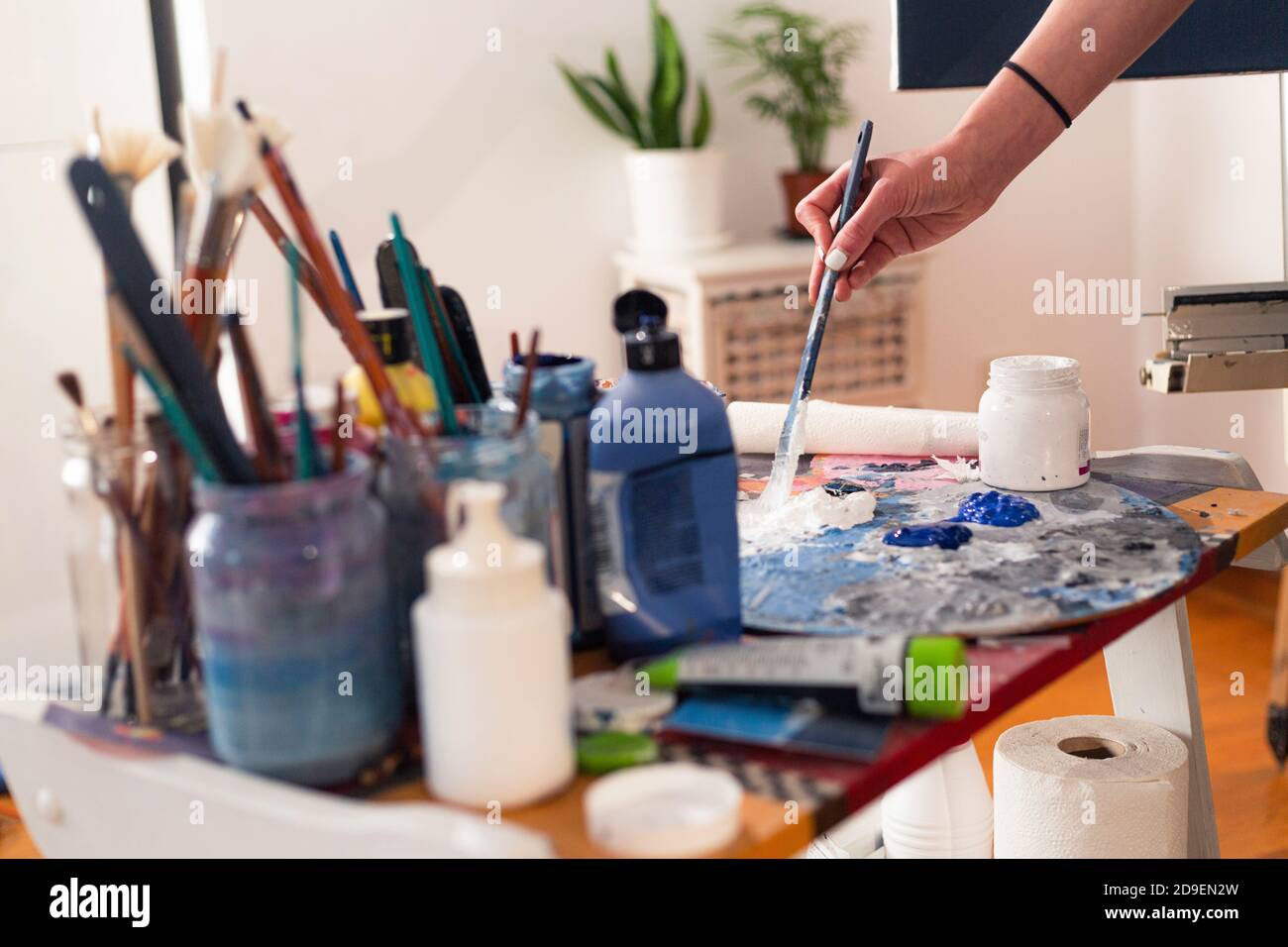 La main du peintre sent de la peinture sur une palette dans son studio. Les pots de peinture et la brosse à peinture sont dans des pots sur le côté. Banque D'Images