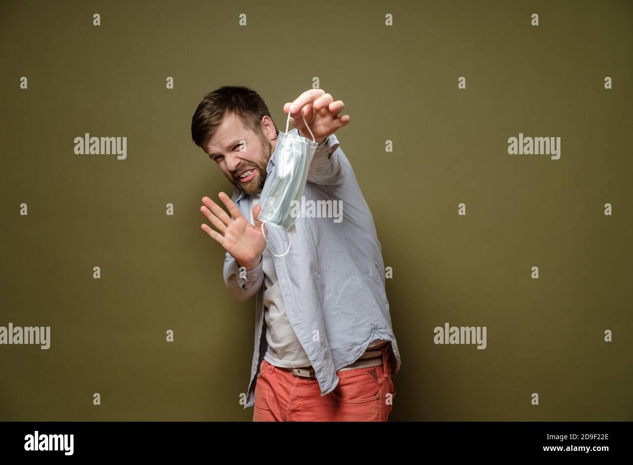 Un homme grinçant, effrayé tient un masque médical utilisé avec deux doigts et montre un geste d'arrêt. Hystérie due à la pandémie. Banque D'Images