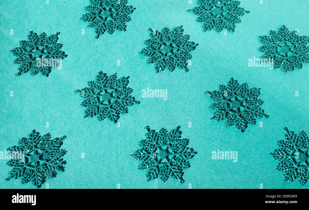 L'arrière-plan est turquoise avec des flocons de neige décoratifs turquoise et brillants. De nombreux flocons de neige sont disposés selon un motif. Photo avec thèmes de Noël. Banque D'Images