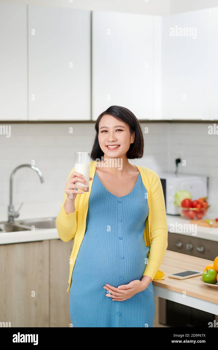 Femme enceinte boit le lait sur la cuisine maison. Banque D'Images