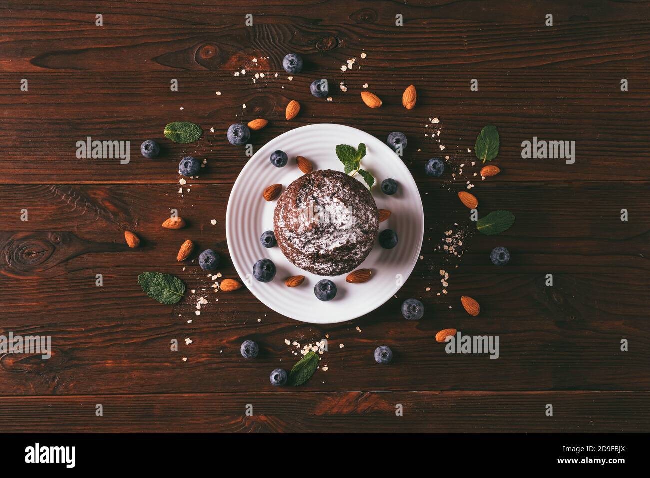 Chocolat muffin brownie sur plaque blanche parmi les bleuets et les amandes épars sur table en bois, vue du dessus. Banque D'Images